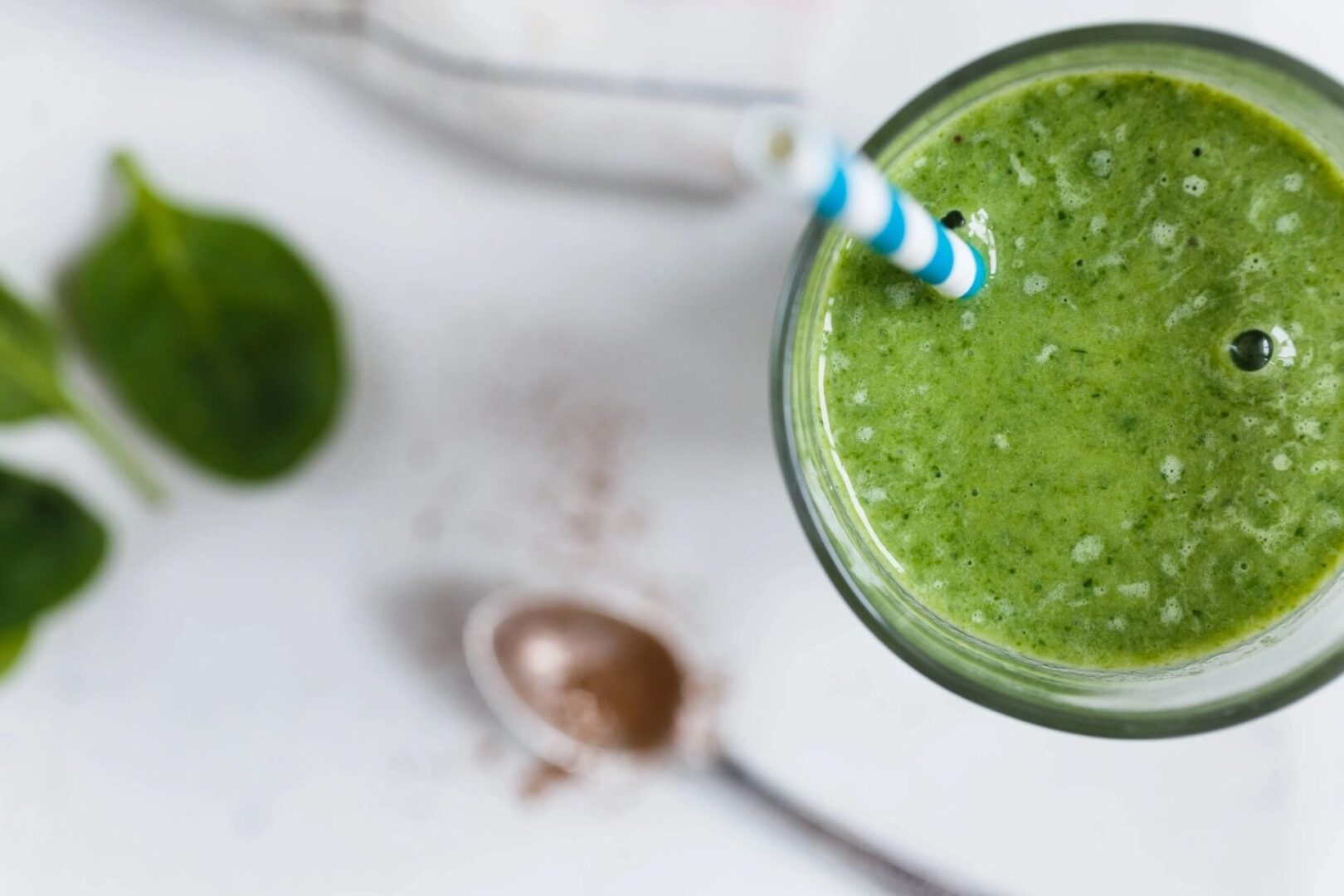 A green smoothie in a glass with a straw.