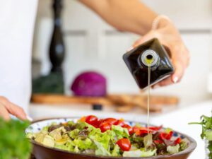 A person pouring olive oil on salad in bowl.